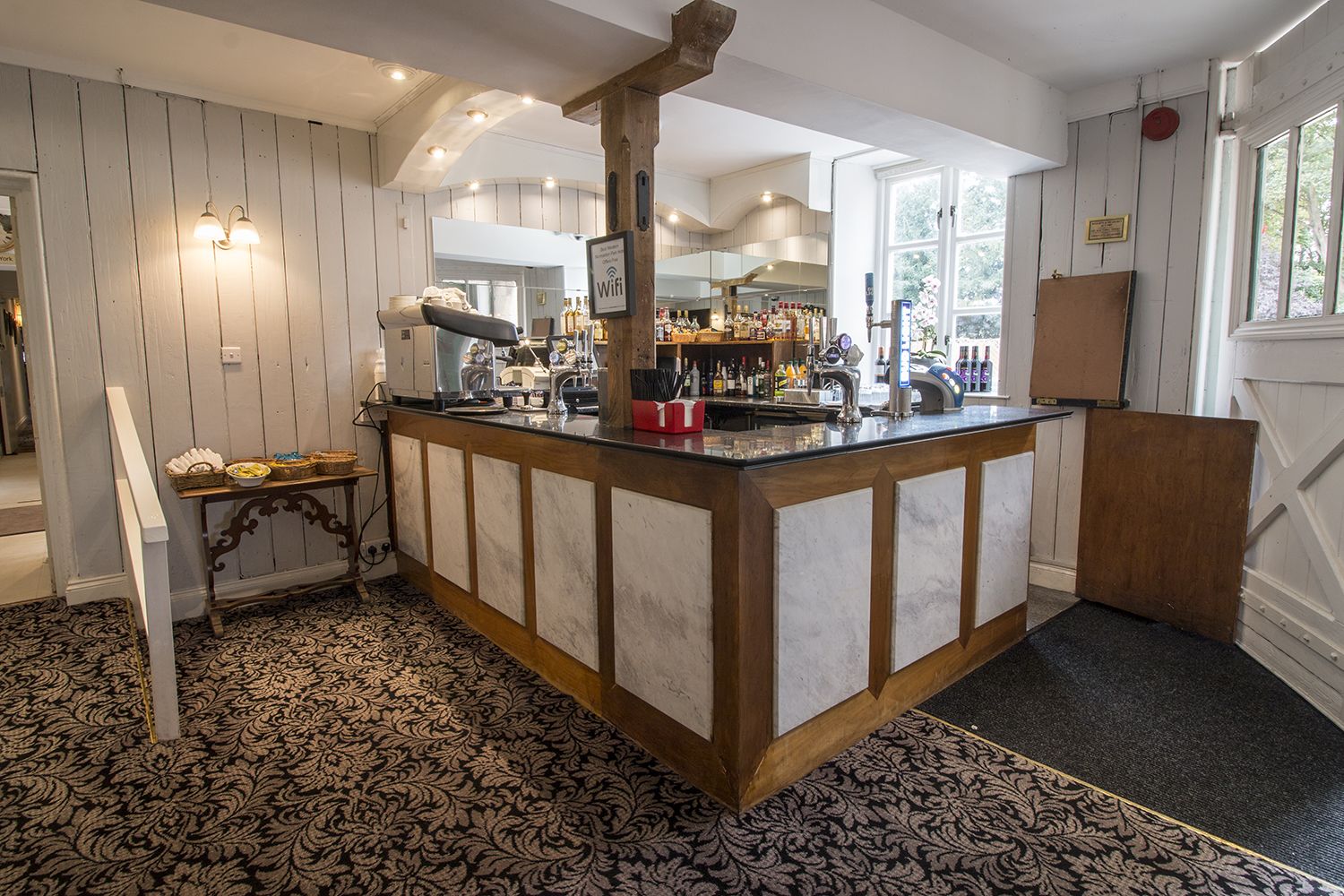 A bar area with a wooden counter, a minibar, and a view of the kitchen in the background.