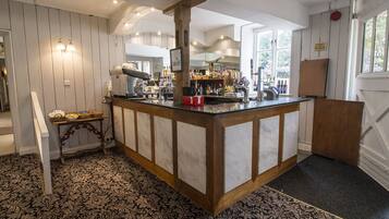 A bar area with a wooden counter, a minibar, and a view of the kitchen in the background.