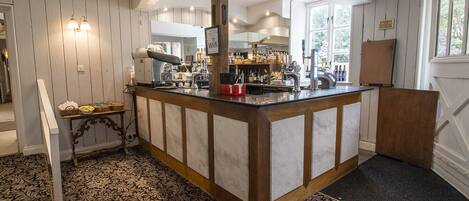 A bar area with a wooden counter, a minibar, and a view of the kitchen in the background.