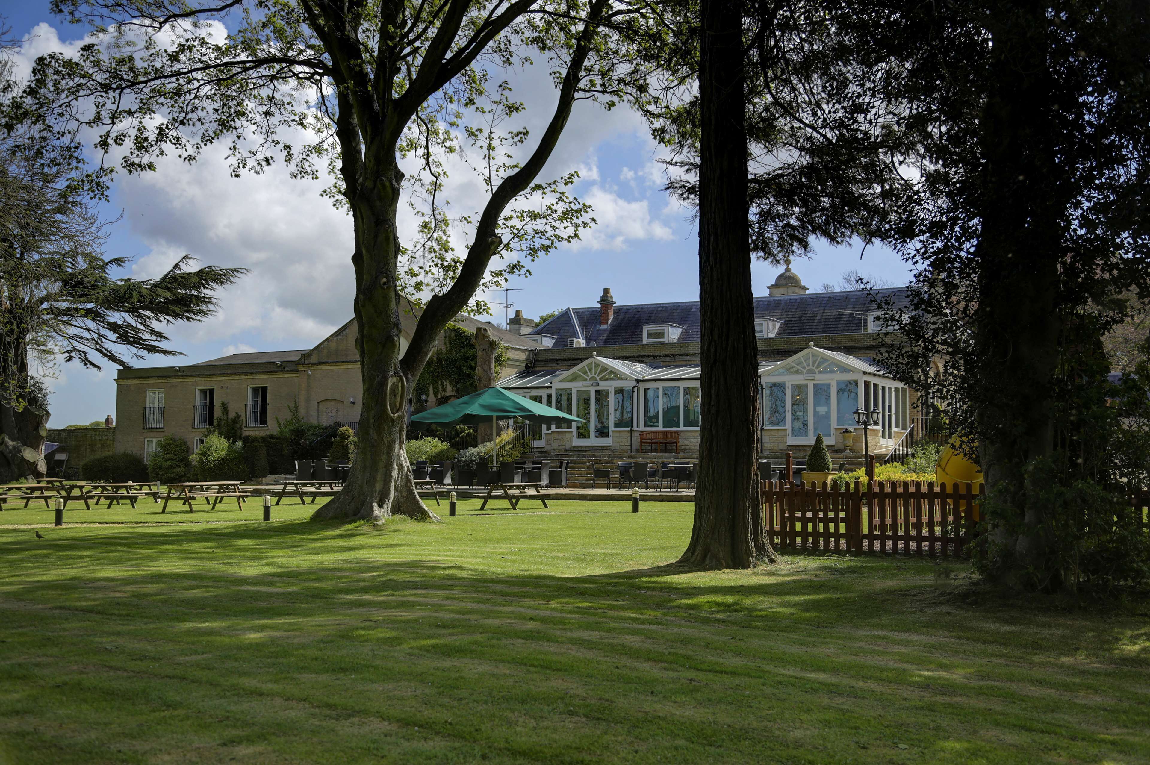 A park with picnic tables, a gazebo, and a building with a large window and a green umbrella.