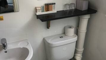 A small bathroom with a sink, toilet, and a shelf with toiletries.