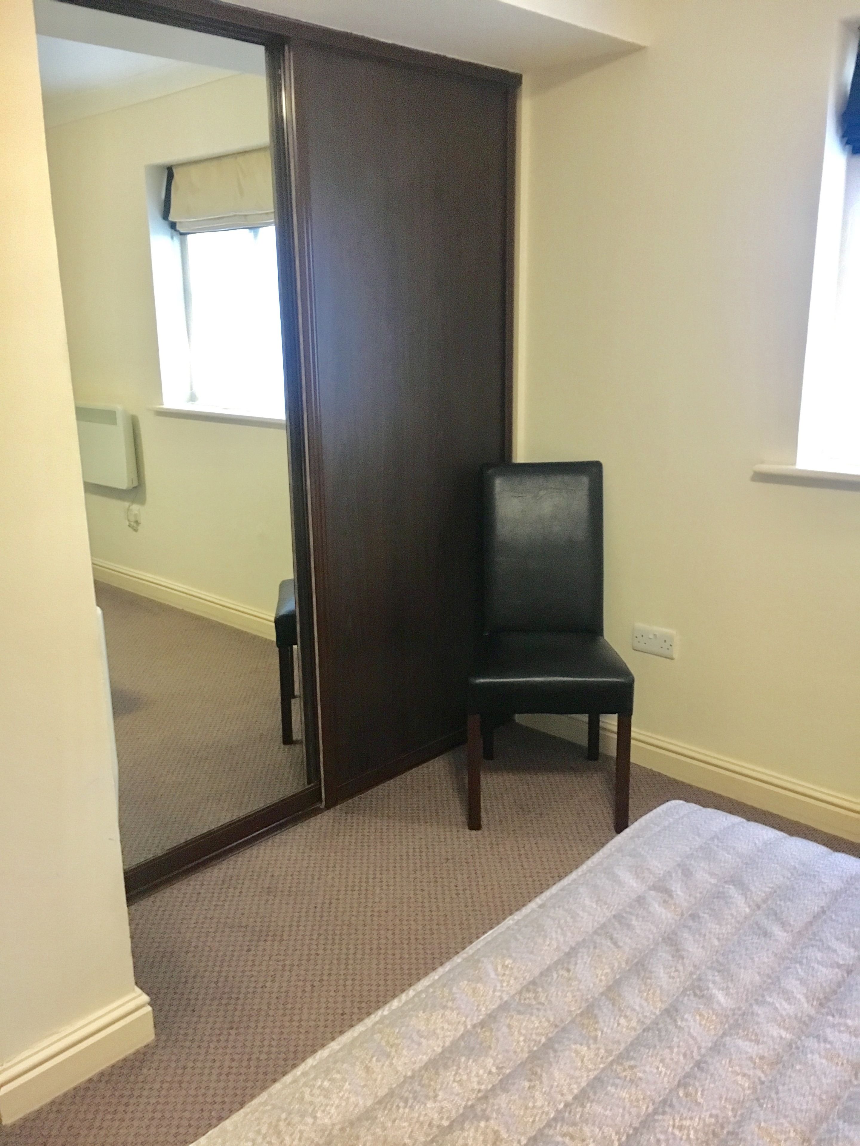 A bedroom with a bed, a chair, a sliding door, and a window.