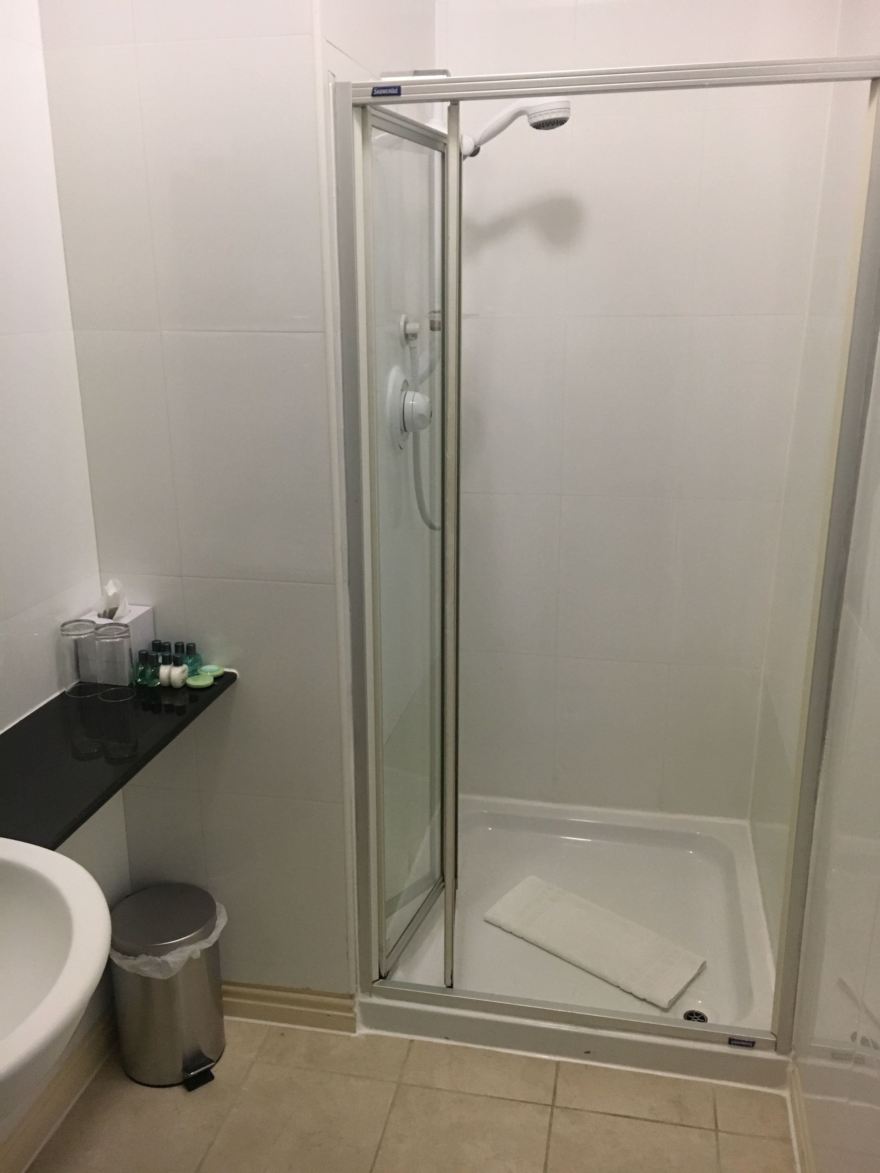 Eine begehbare Duschkabine mit Duschbrause, ein schwarzer Waschtisch mit Toilettenartikeln und ein Mülleimer.