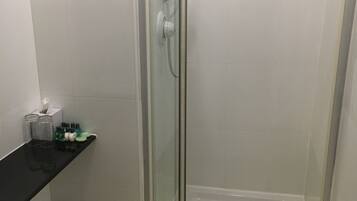 Eine begehbare Duschkabine mit Duschbrause, ein schwarzer Waschtisch mit Toilettenartikeln und ein Mülleimer.