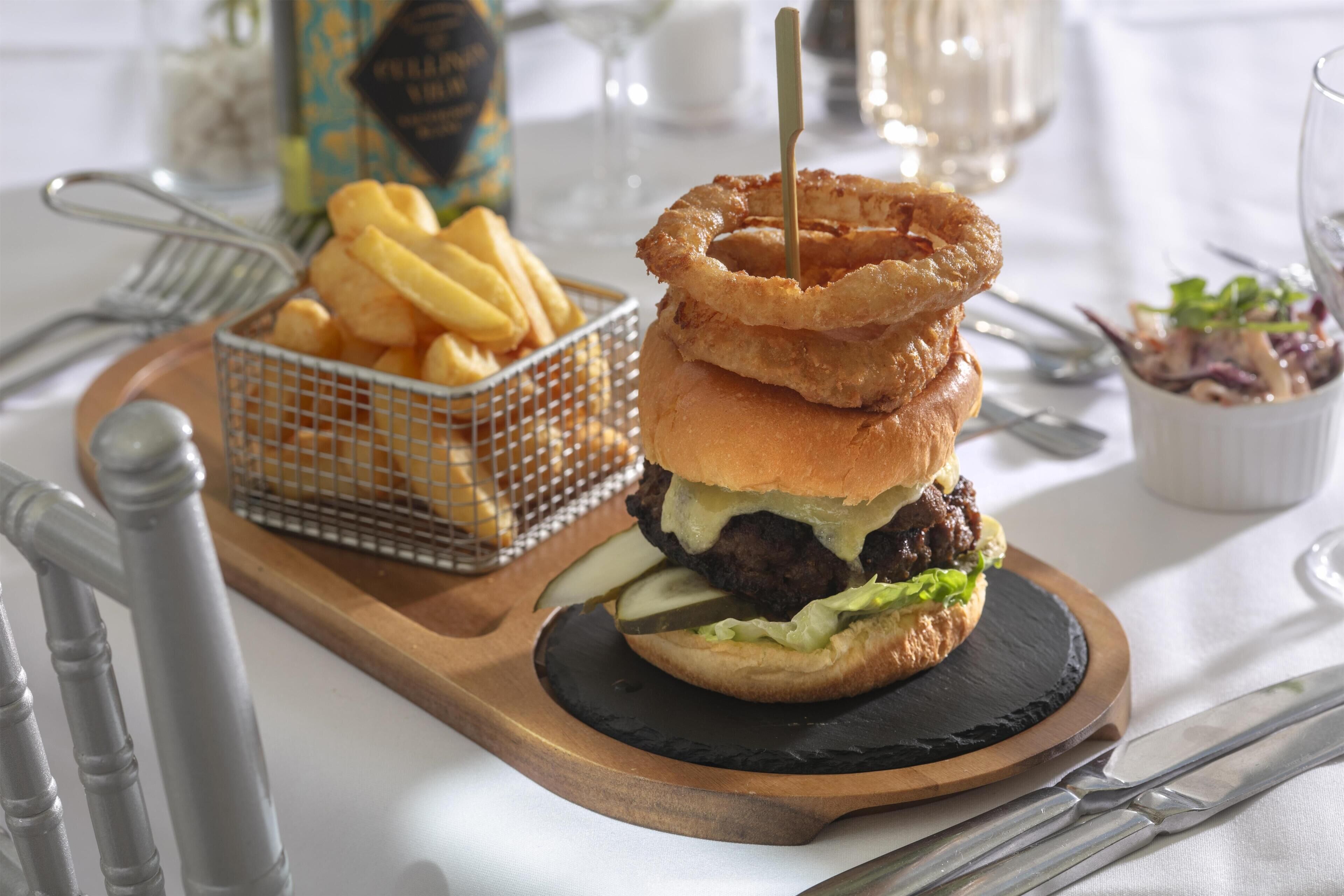 Una hamburguesa con aros de cebolla, papas fritas y una ensalada pequeña, todo sobre una tabla de madera.
