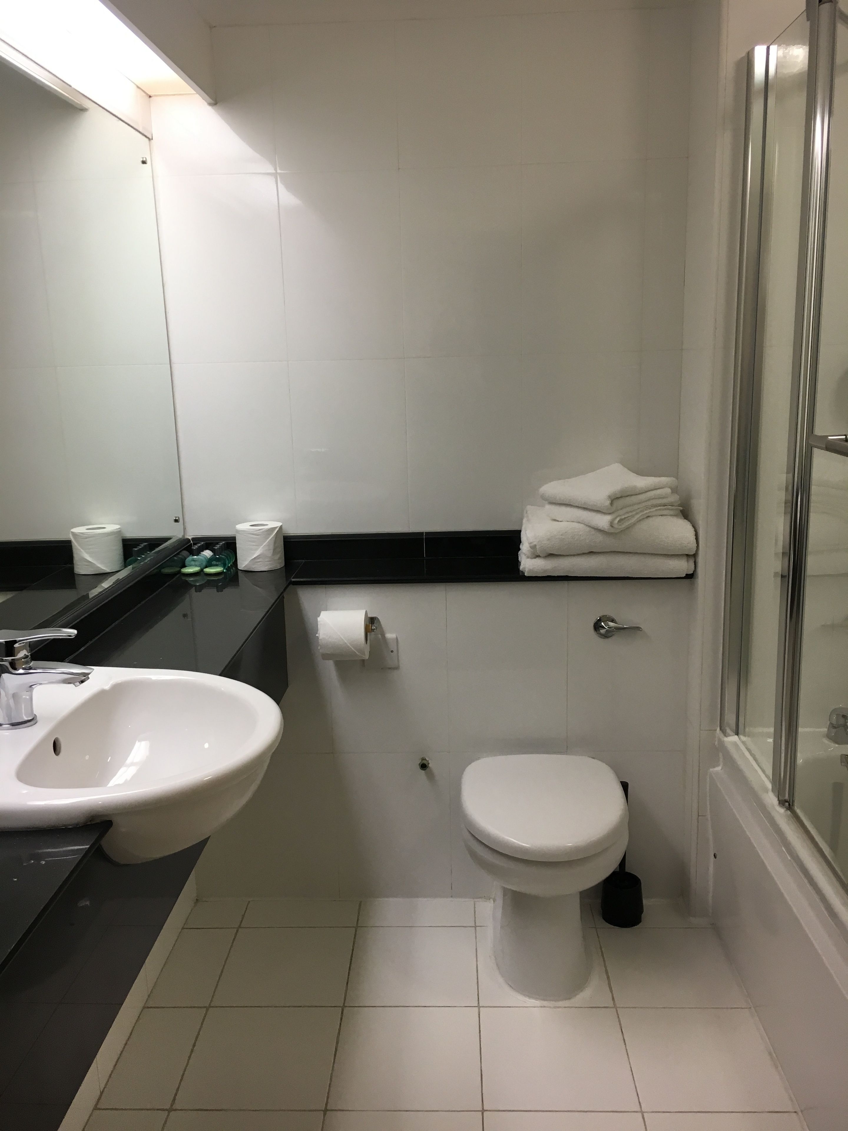 Un baño pequeño con lavamanos blanco, inodoro y cabina de ducha con mampara de vidrio.
