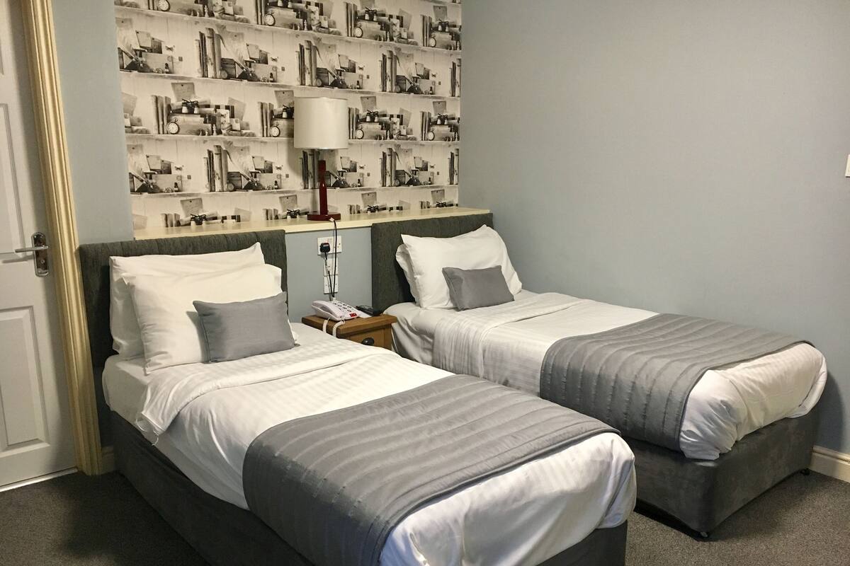 Hotellihuone, jossa on kaksi sänkyä, yöpöytä lampun kanssa ja seinä, jossa on kellokuvio.