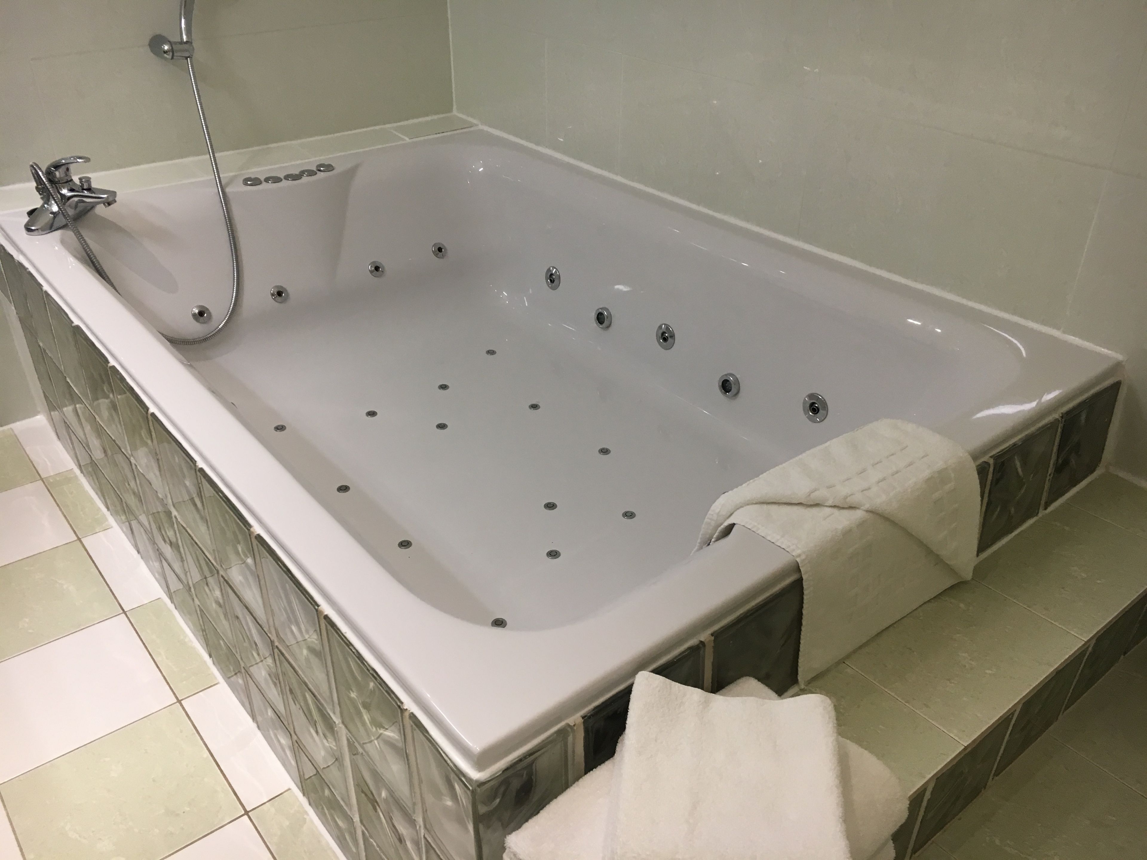 Une grande baignoire rectangulaire dotée d’un pommeau de douche et de plusieurs trous d’évacuation.