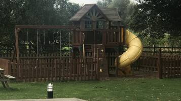 Children can play on the playground equipment, surrounded by picnic tables.