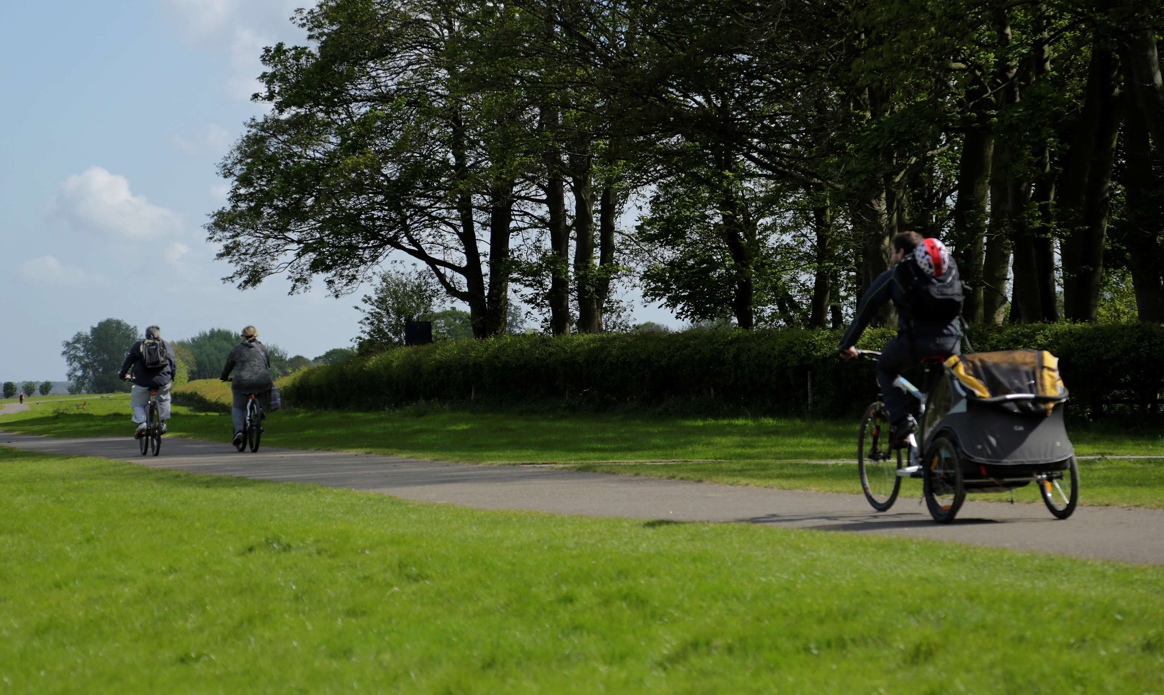 Un chemin pavé, bordé de verdure et d’arbres, où l’on peut apercevoir des cyclistes.