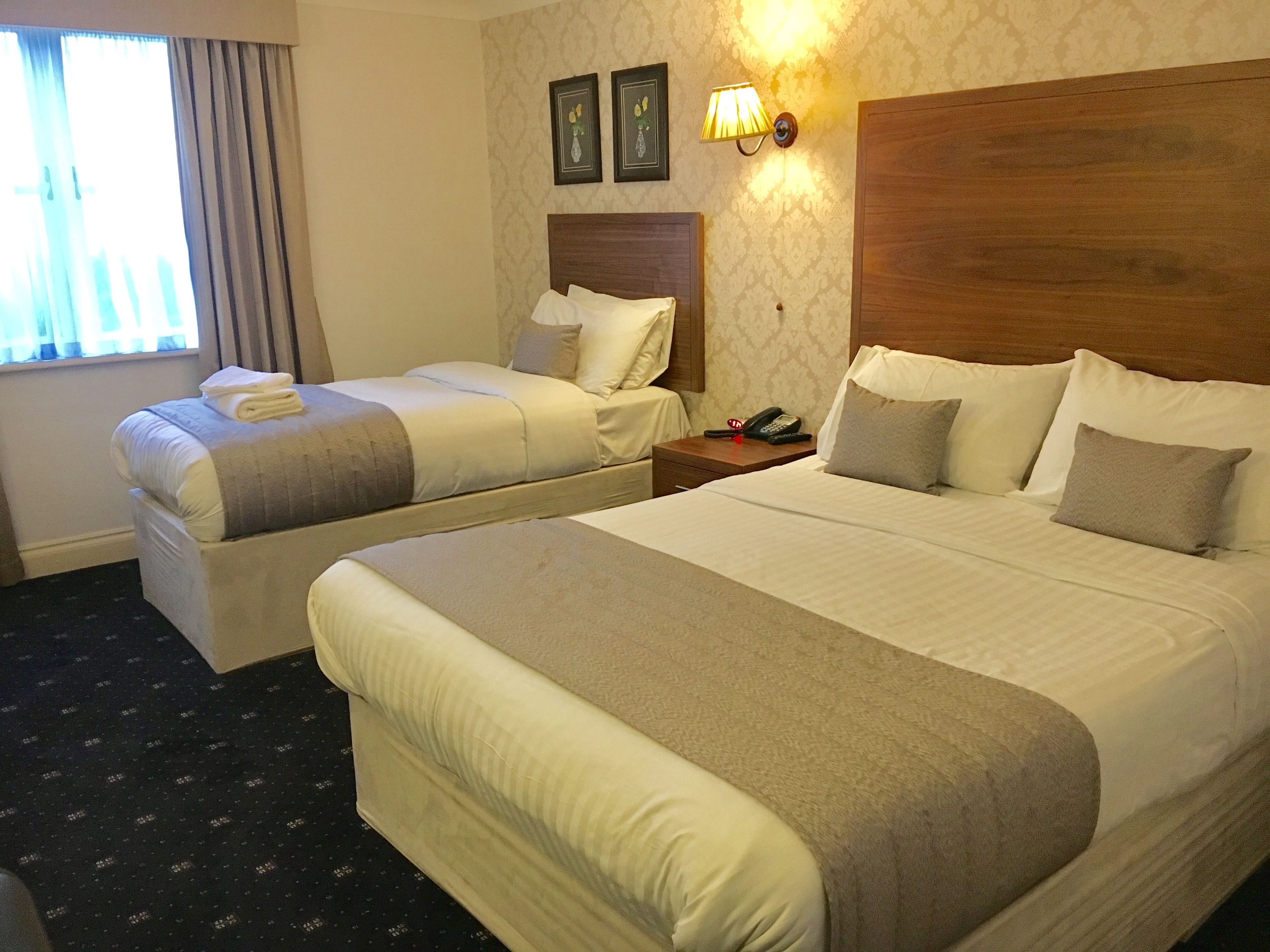 Una habitación de hotel con dos camas, una mesita de noche con un teléfono y una lámpara de pared.