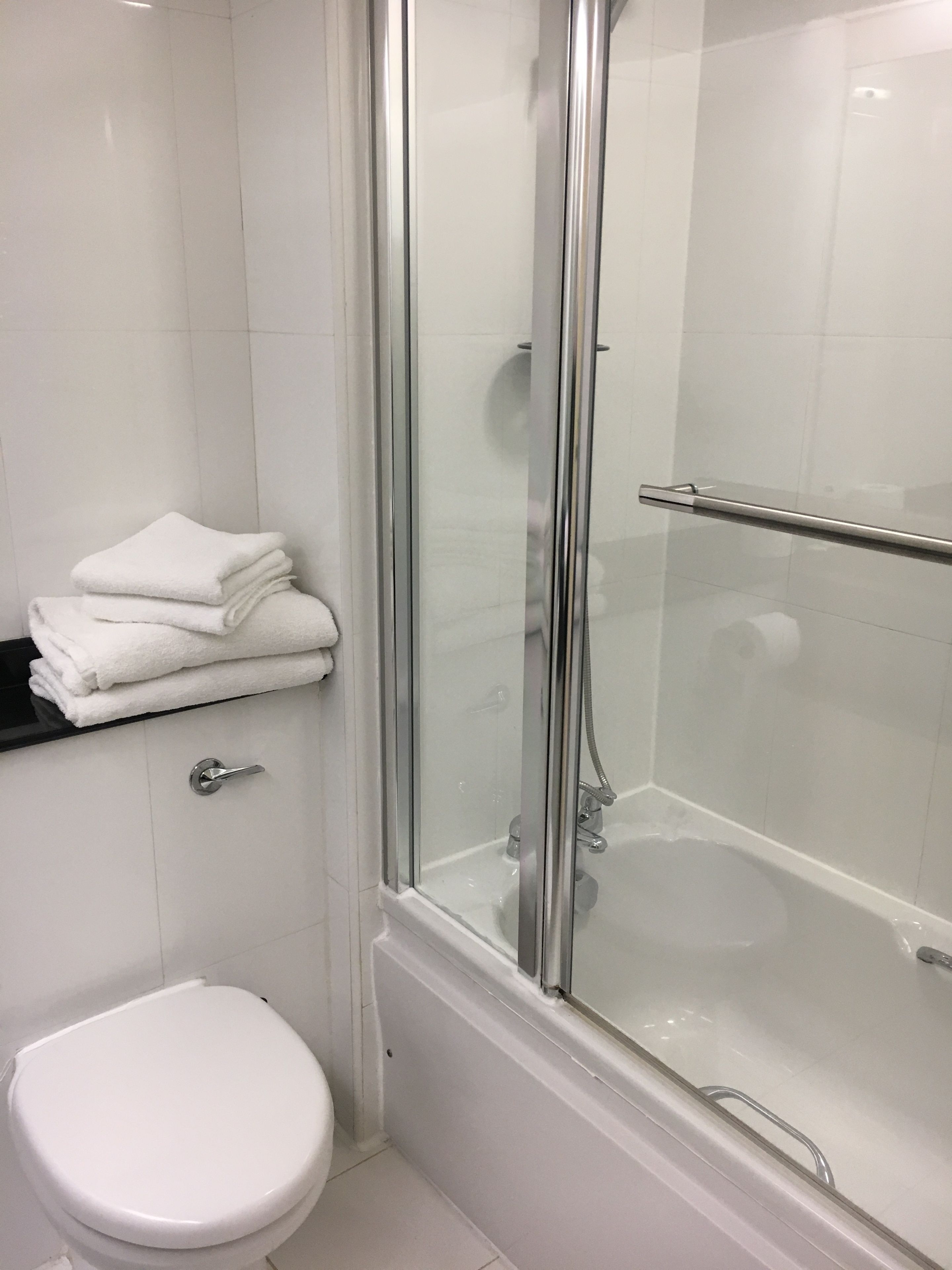 A modern bathroom with a glass-enclosed shower, a white toilet, and a stack of white towels on a black countertop.