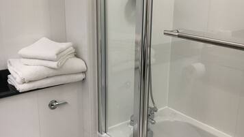 A modern bathroom with a glass-enclosed shower, a white toilet, and a stack of white towels on a black countertop.