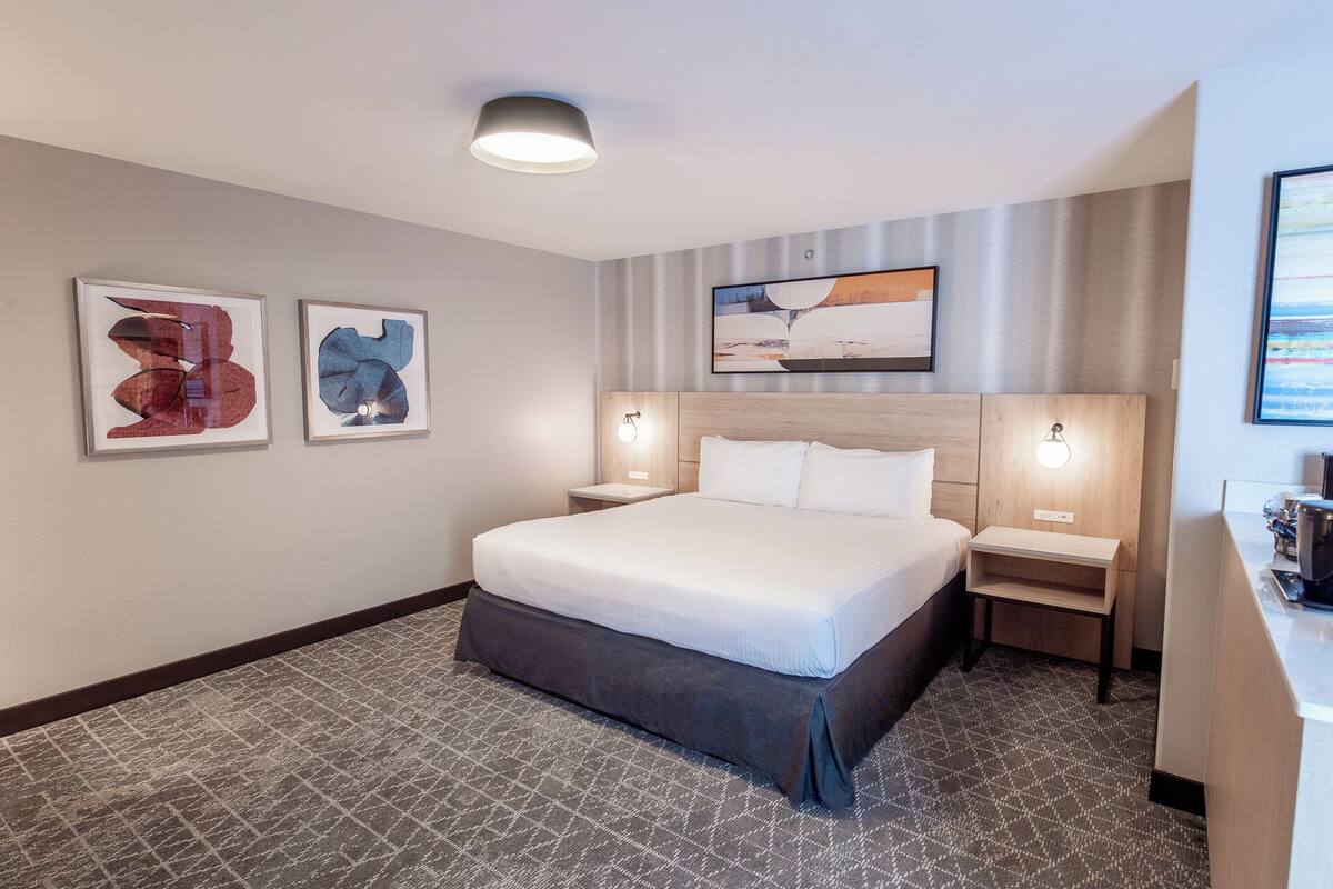 Une chambre d’hôtel avec un grand lit, deux tables de chevet, une tête de lit et des œuvres d’art accrochées aux murs.
