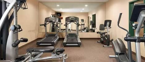 Un gimnasio con cintas de correr, máquinas de pesas y un espejo grande.