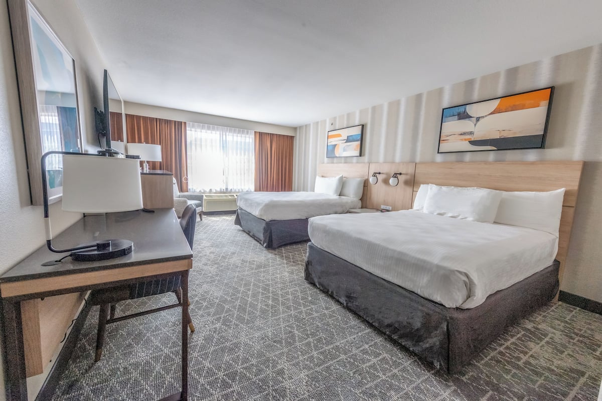 Une chambre d’hôtel avec deux lits, un bureau avec une lampe, une télévision et un tableau au mur.