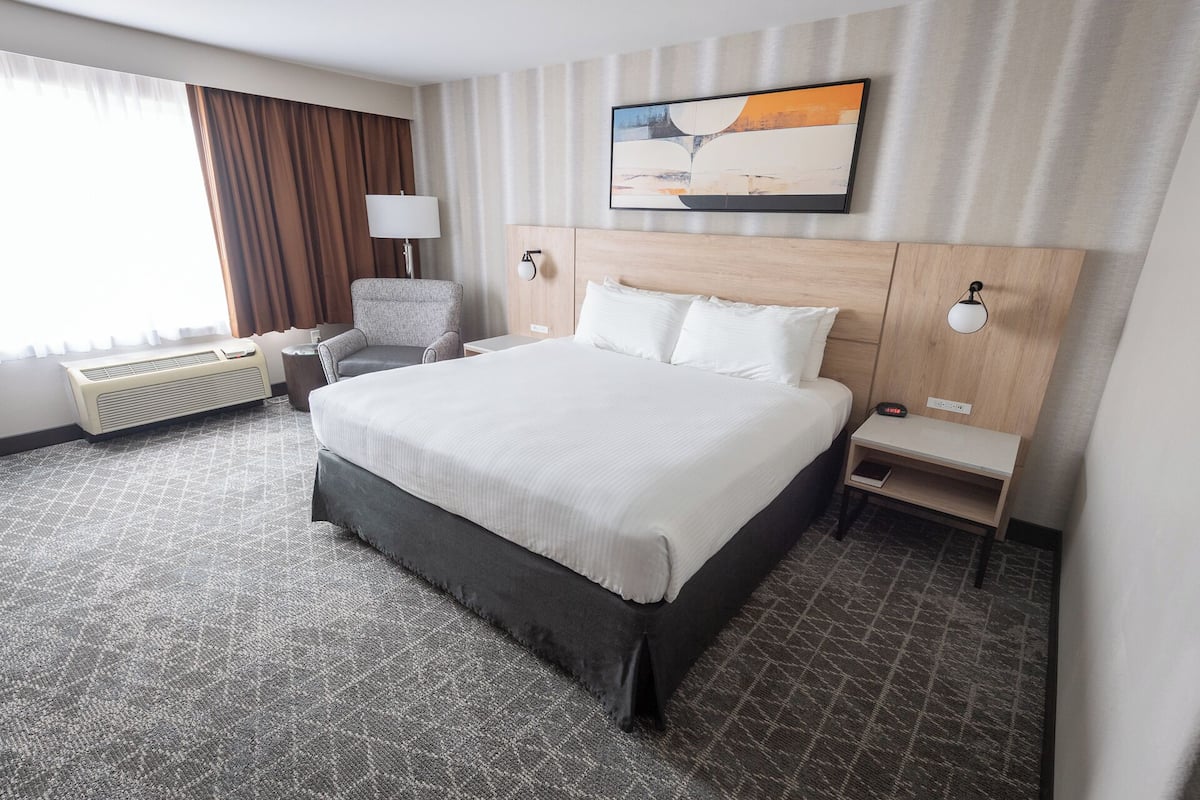 Une chambre d’hôtel avec un grand lit, une chaise, une table de chevet, une lampe et une œuvre d’art accrochée au mur.