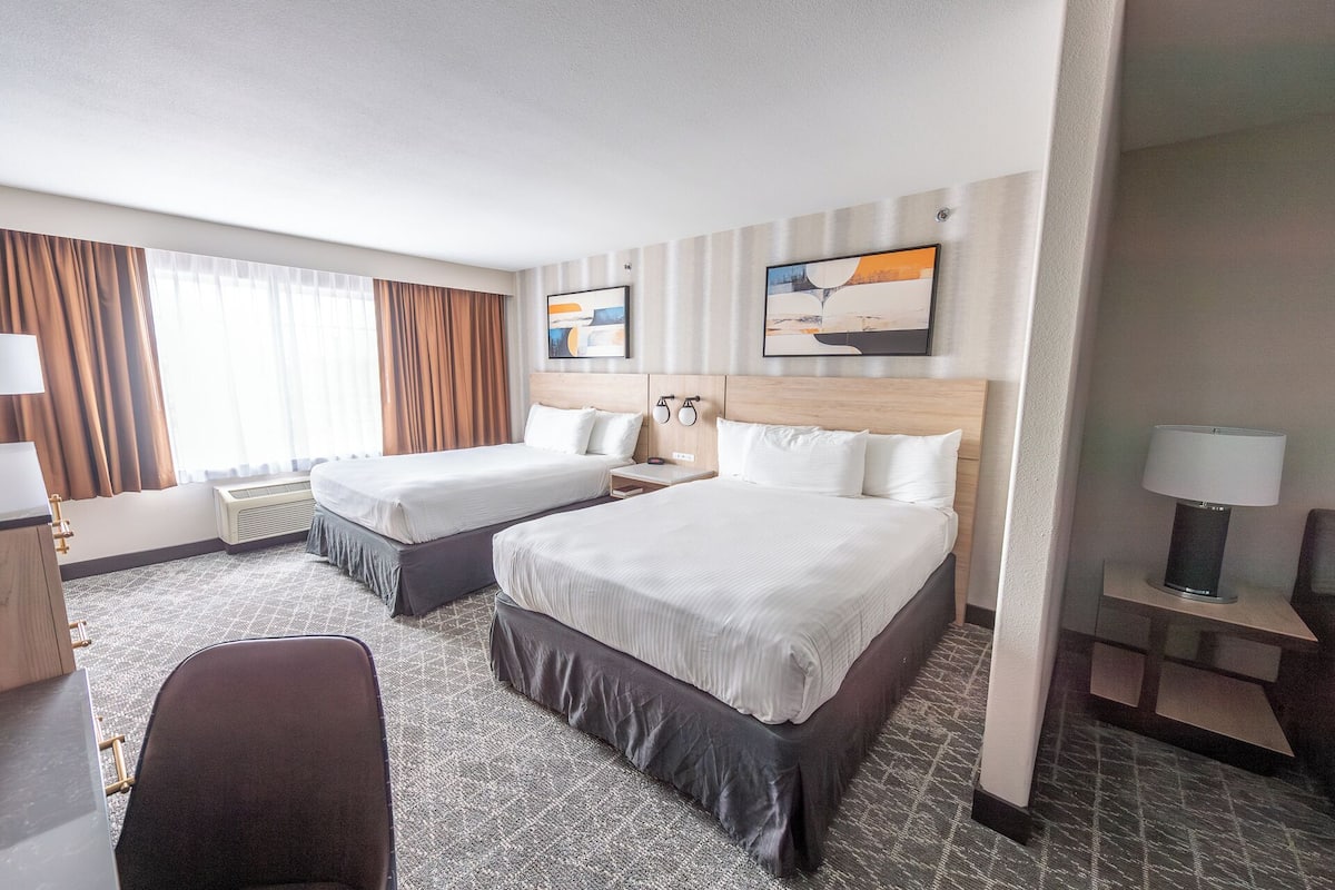 Une chambre d’hôtel avec deux lits, un bureau, une chaise et un téléviseur.