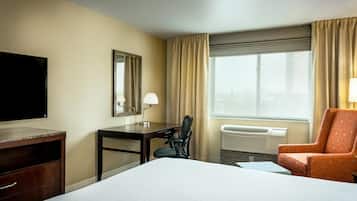 A hotel room with a bed, desk, chair, television, and a window with curtains.
