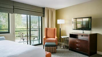 Ein Hotelzimmer mit Bett, Sessel, Fernseher, Kommode und einem Balkon mit Tisch und Stühlen.
