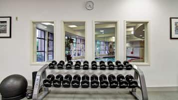 A gym with a wall-mounted clock, large windows, and a rack of dumbbells.