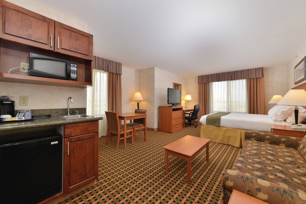 A hotel room with a kitchenette, a bed, a desk, a chair, and a sofa.