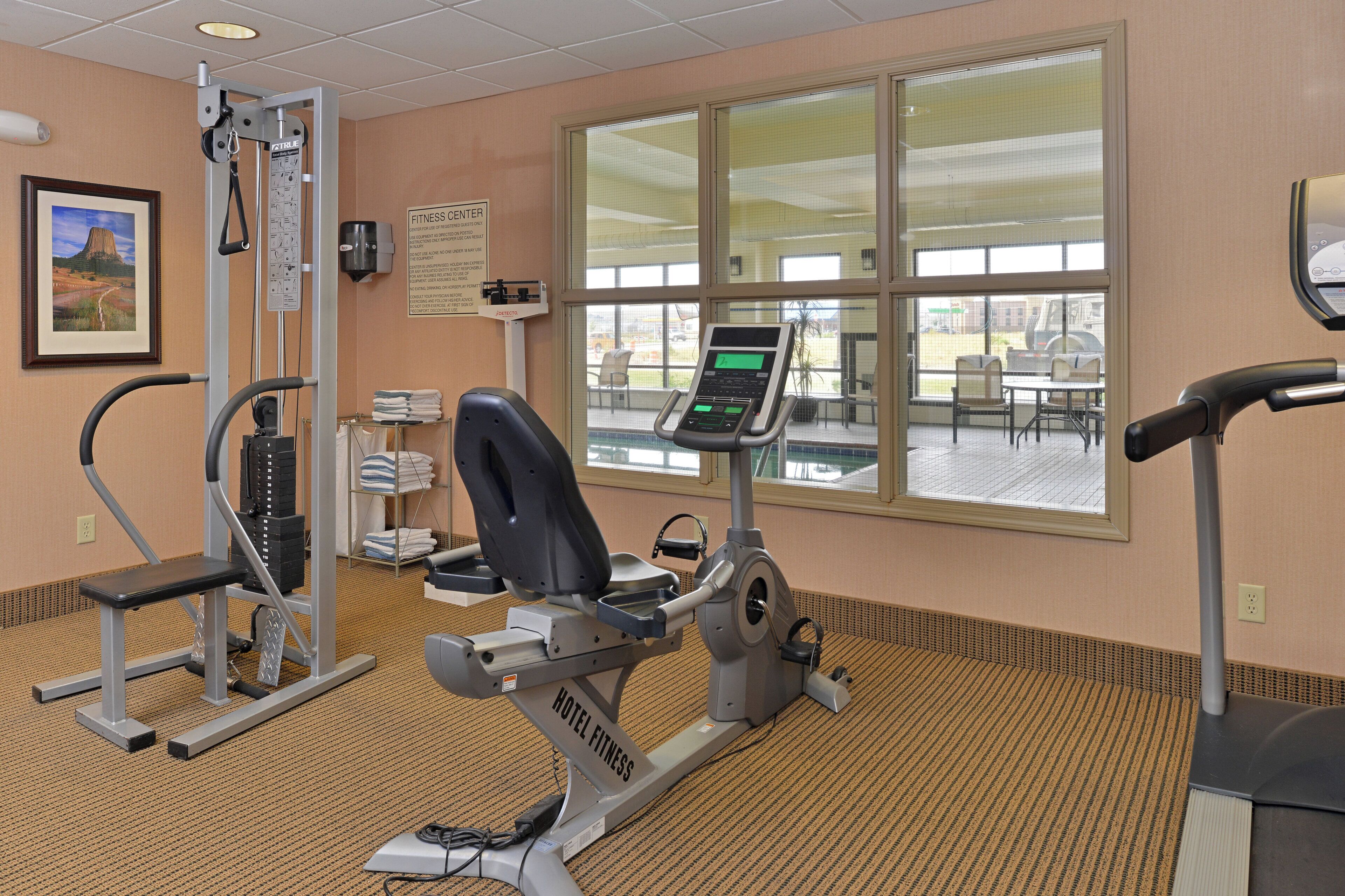 A hotel fitness center with exercise equipment, a treadmill, and a large window providing a view of the outside.