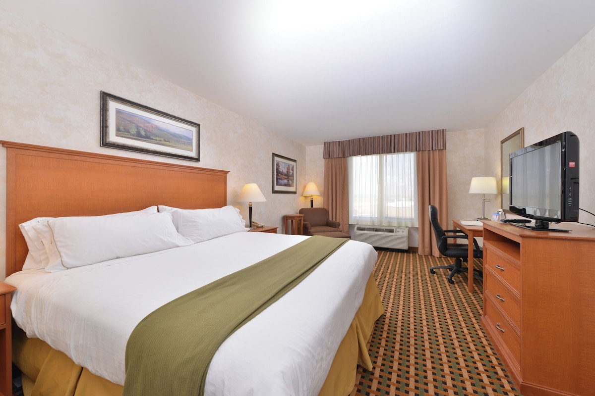A hotel room with a large bed, a desk with a computer, a television, and a window with curtains.