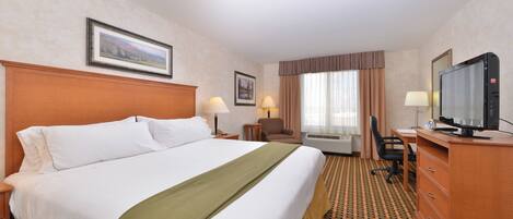 A hotel room with a large bed, a desk with a computer, a television, and a window with curtains.