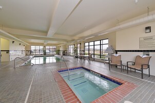 Una piscina interior con suelo de baldosas, una escalera de piscina y una zona de estar con sillas.