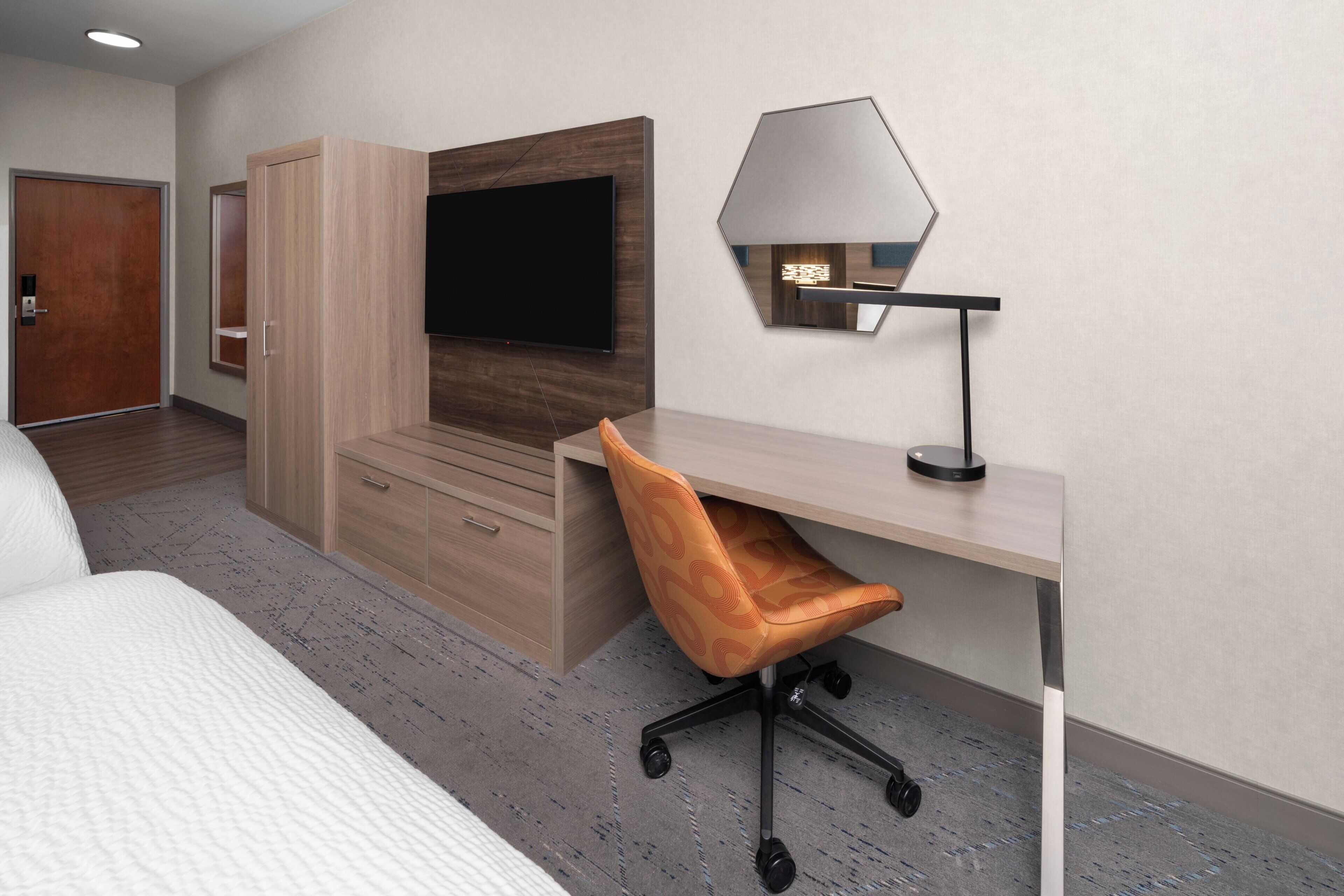 Une chambre d’hôtel avec un lit, un bureau avec une chaise, une télévision et une lampe.