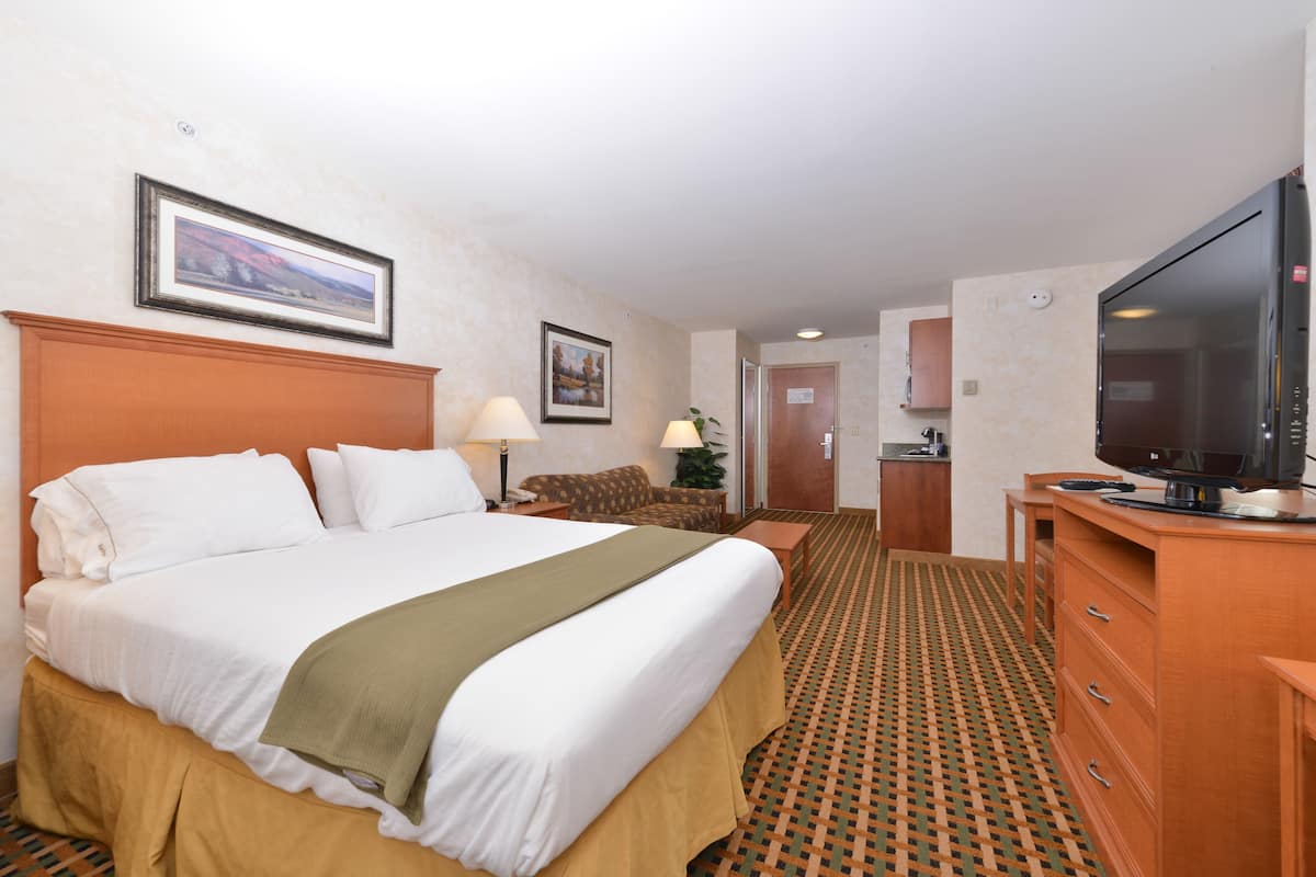 A hotel room with a large bed, a television, a desk, and a chair.