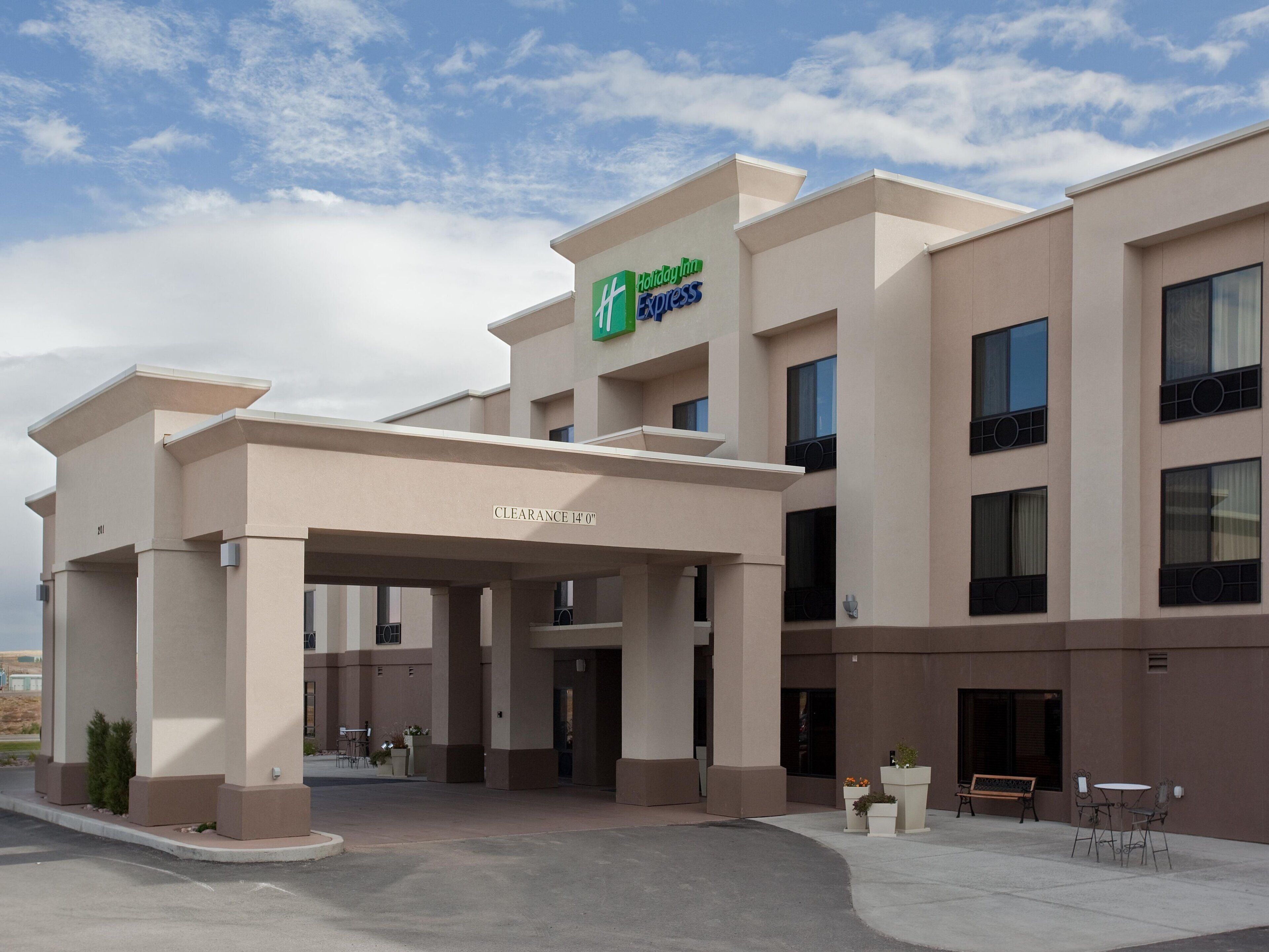 A Holiday Inn Express building with a clear entrance, outdoor seating area, and a sign indicating a 14'0' clearance.