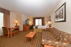 A hotel room with a bed, a sofa, a desk with a chair, a TV, and a lamp.
