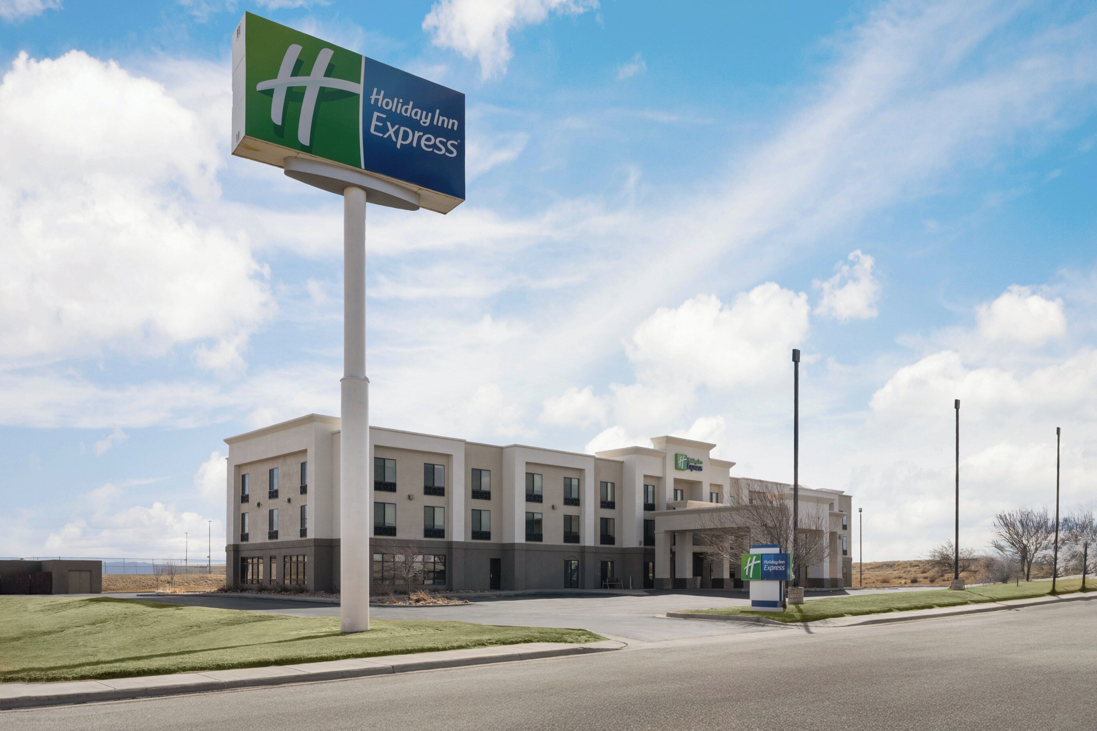 A Holiday Inn Express hotel with a modern building facade, a large parking lot, and a clear sky.