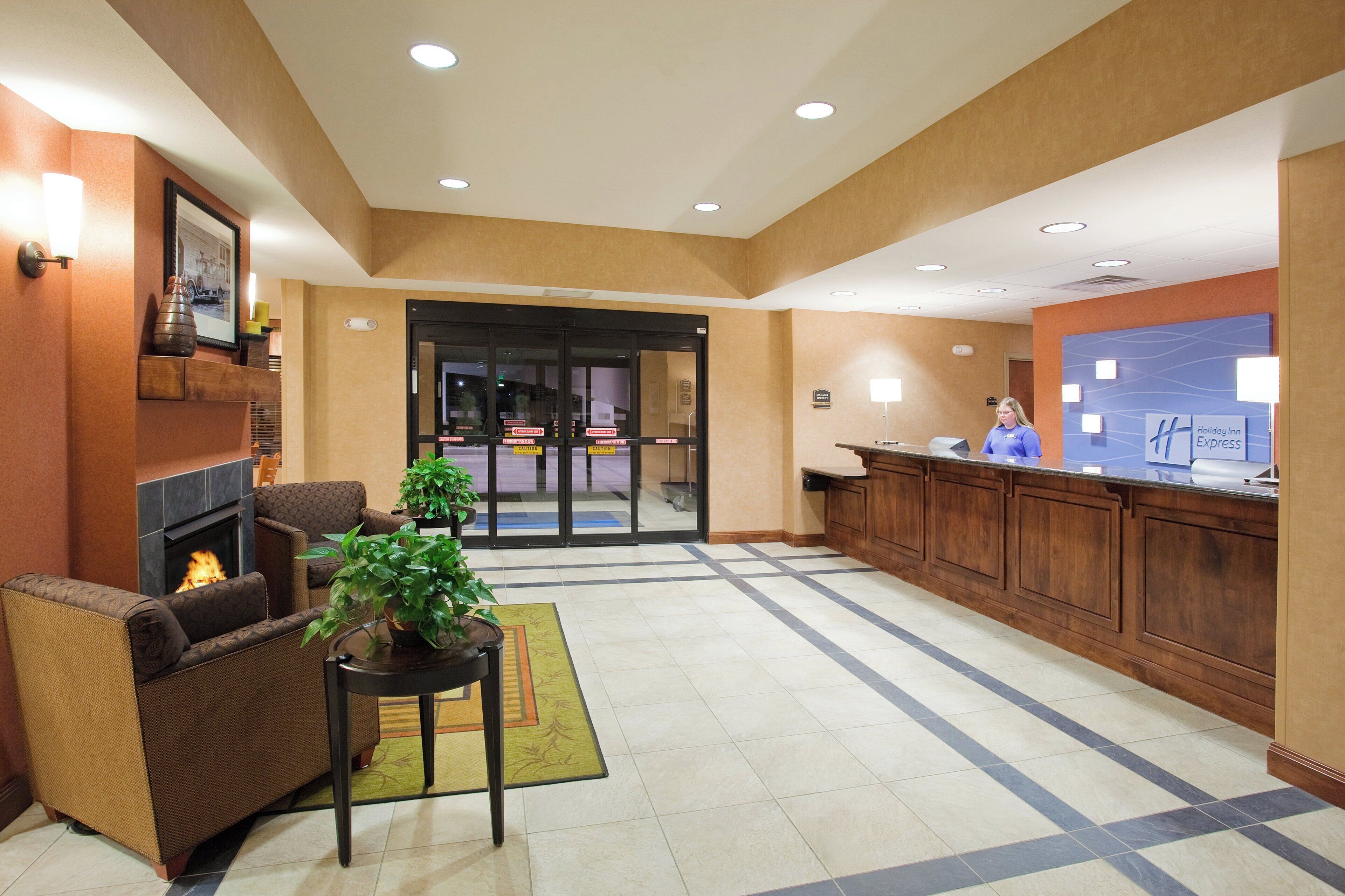 A lobby with a fireplace, seating area, reception desk, and a large glass door entrance.