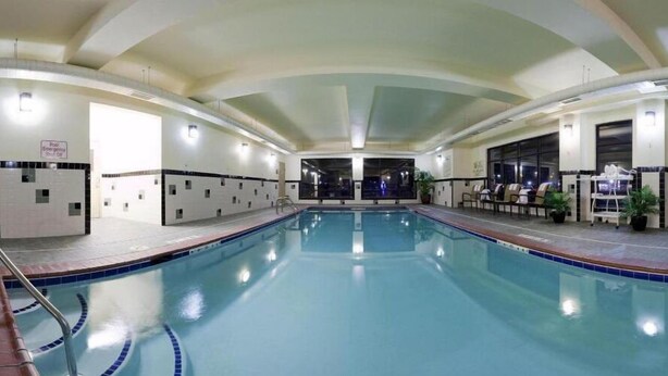 A large indoor swimming pool with clear lanes, a poolside area with chairs, and a sign indicating an emergency exit.