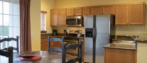 A compact kitchen with wooden cabinets, a stainless steel refrigerator, a microwave, and a stove.