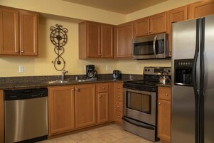 Una cocina con armarios de madera, electrodomésticos de acero inoxidable, lavavajillas y cafetera.