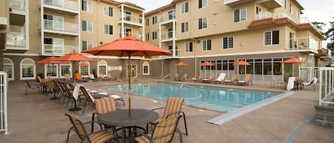 A hotel with a swimming pool, outdoor seating, and multiple balconies.