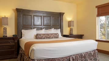 A large bed with a wooden headboard, two bedside tables with lamps, and a window with a view of trees.