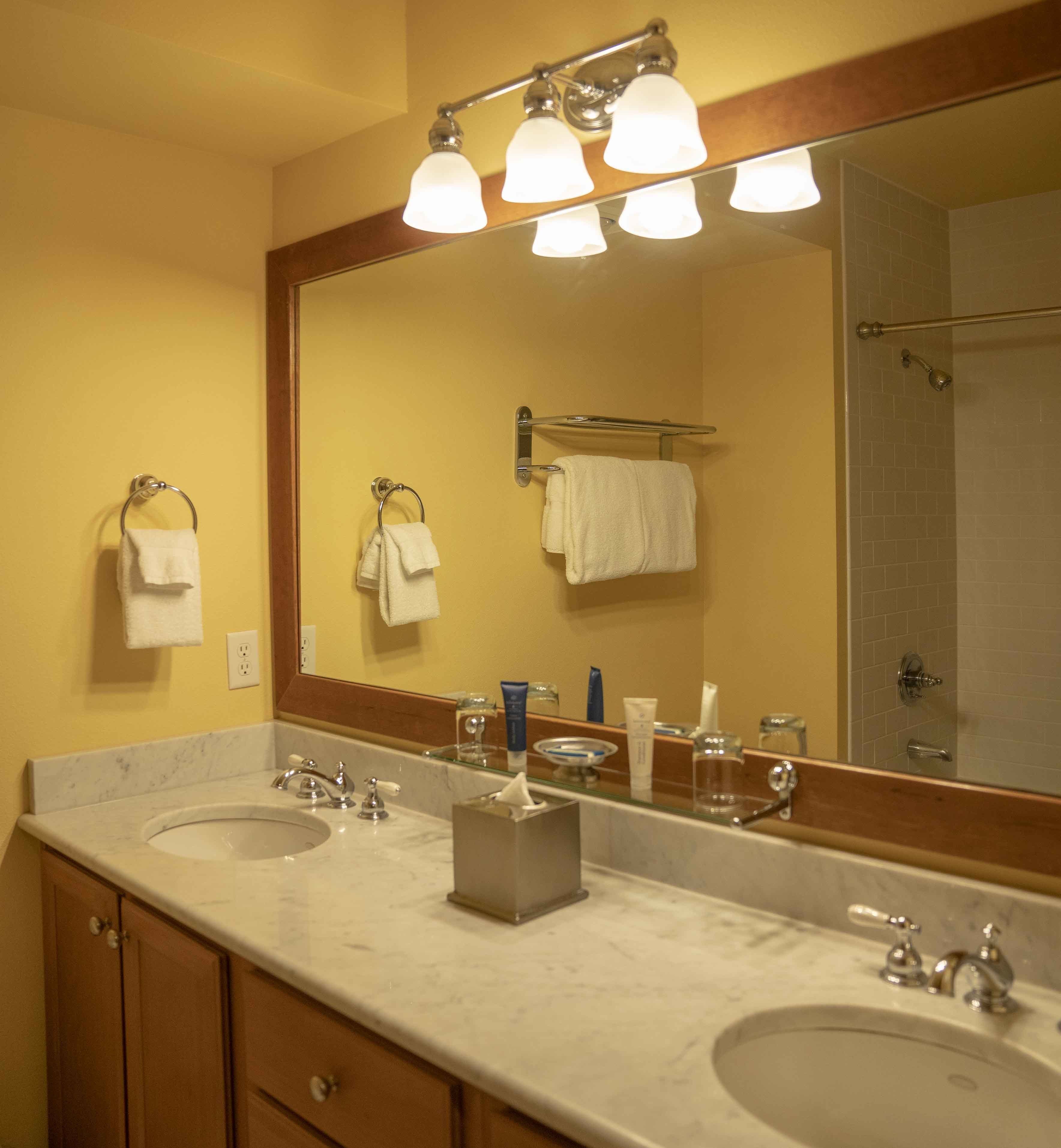 A bathroom with two sinks, a large mirror, and a shower visible in the reflection.