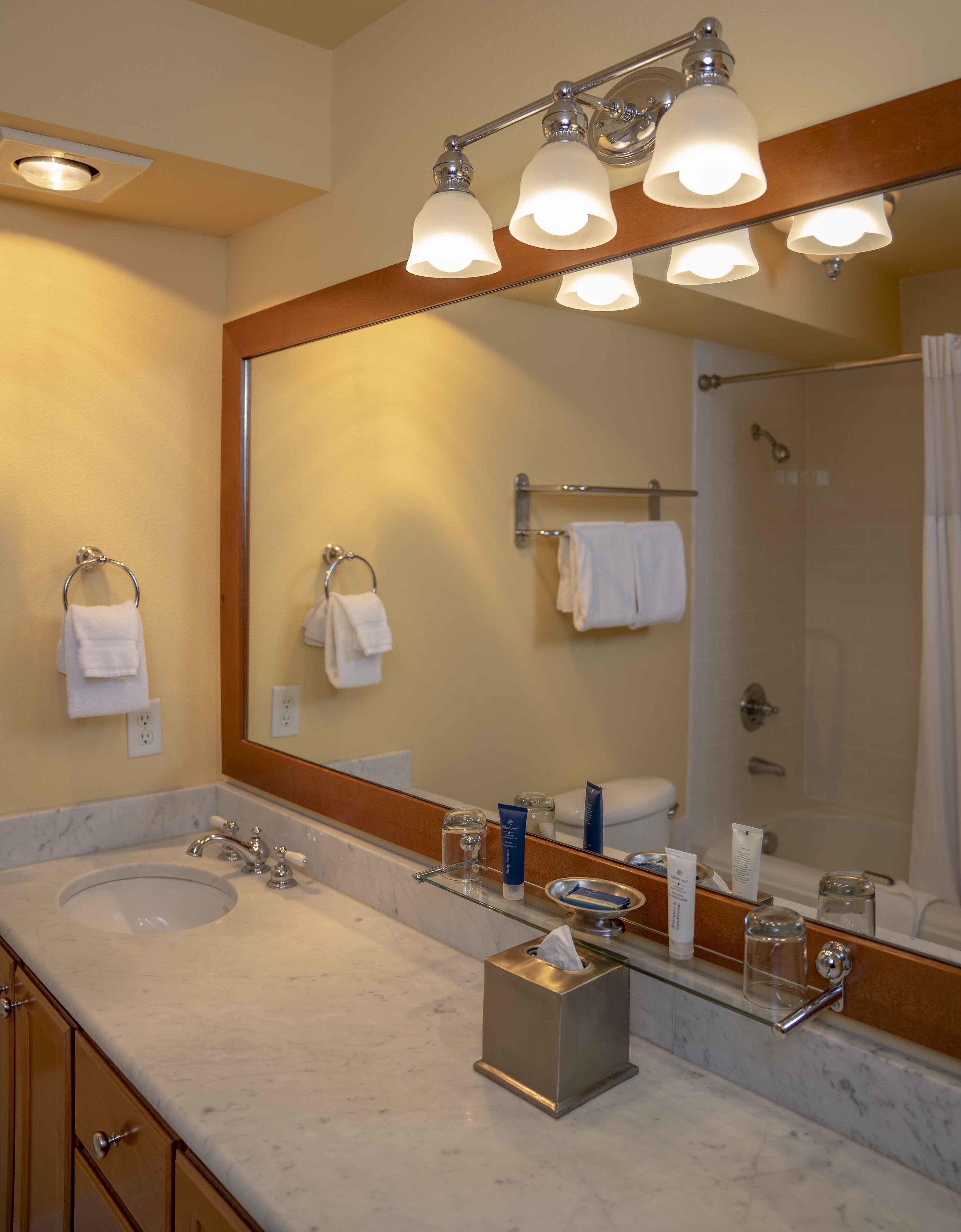 Une salle de bain avec un grand miroir, deux lavabos, une douche et un porte-serviettes.