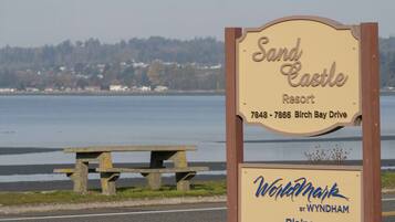 A sign for Sand Castle Resort with a view of the water and a picnic table.