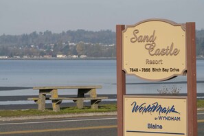 A sign for Sand Castle Resort with a view of the water and a picnic table.