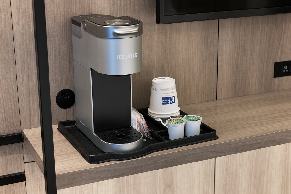 A Keurig coffee machine with a tray holding a disposable cup and two travel-sized coffee cups.