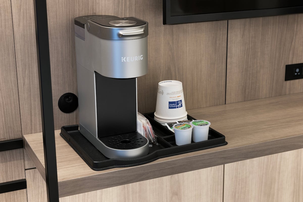 A Keurig coffee machine with a tray holding a disposable cup and two travel-sized coffee cups.
