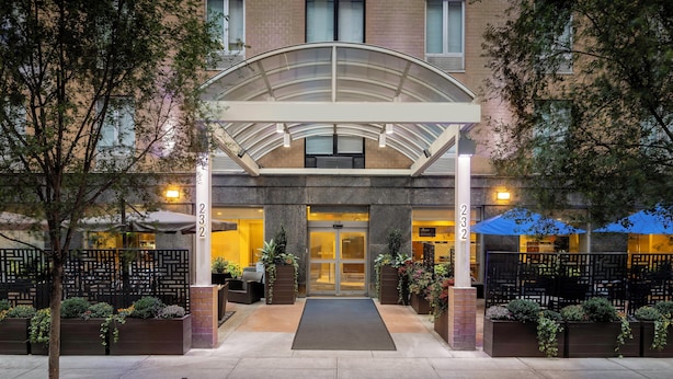 L’entrée d’un hôtel, avec un passage couvert, une façade en briques et des espaces de détente en plein air.