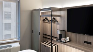Une chambre d’hôtel moderne équipée d’une grande télévision, d’une machine à café et d’une armoire avec un miroir.