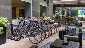 Une rangée de vélos est stationnée sous un auvent, à côté d’un espace de sièges extérieur agrémenté de plantes en pot.